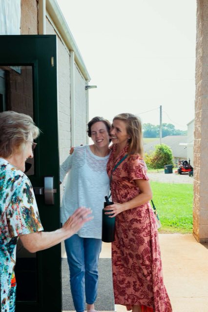 Two women hugging in the doorway while a greeter holds the door