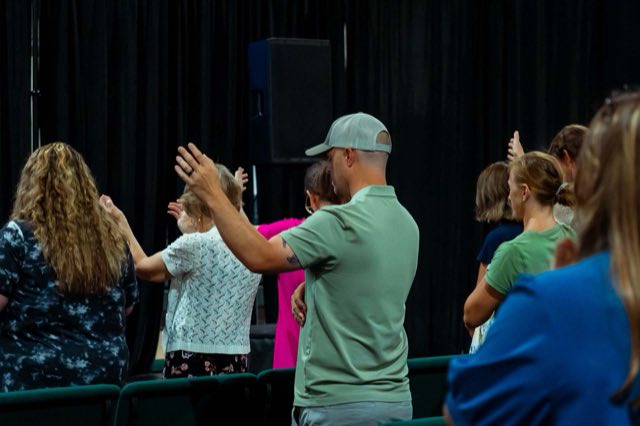 An adult with an arm around a child while the room sings