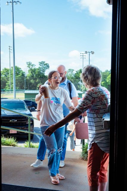 A greeter reaching out to welcome a young woman carrying a coffee