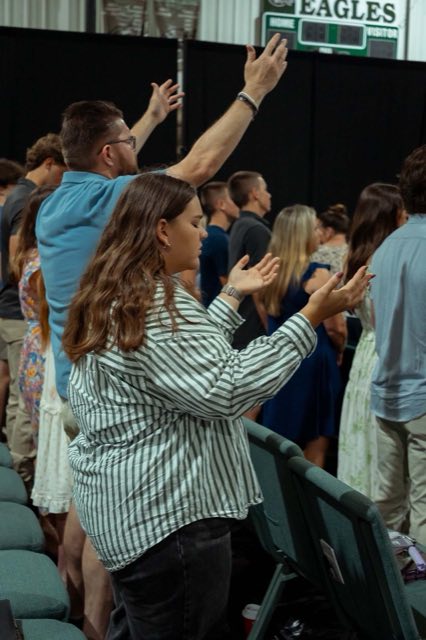 People standing with hands raised during worship in the gym