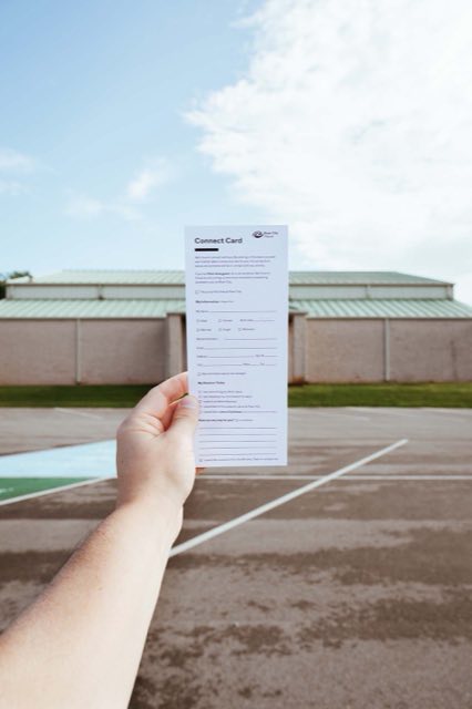 A hand holding a River City Church connect card outside the building