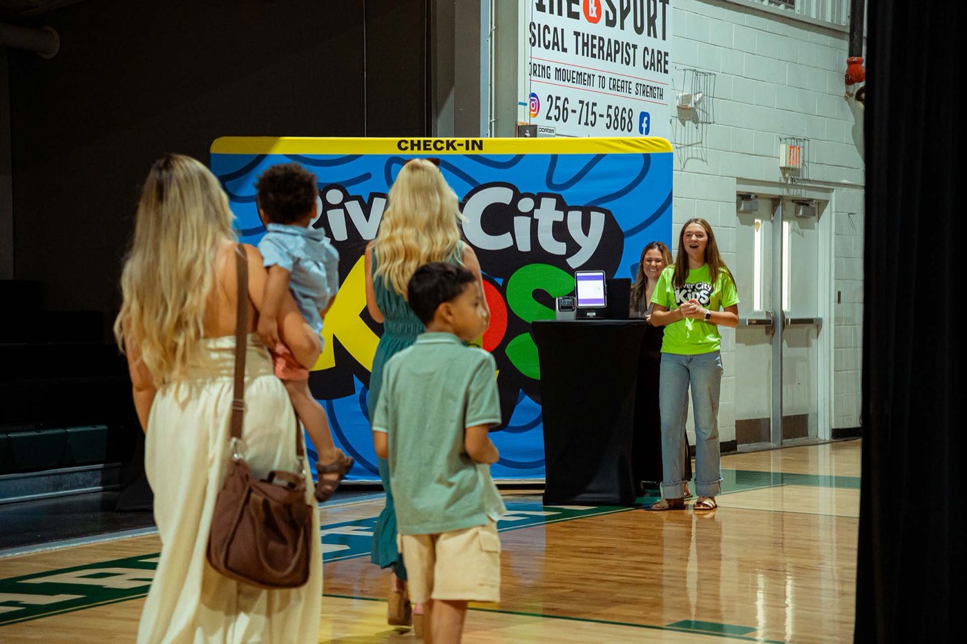 Volunteers in River City Kids shirts welcoming families at the check-in desk