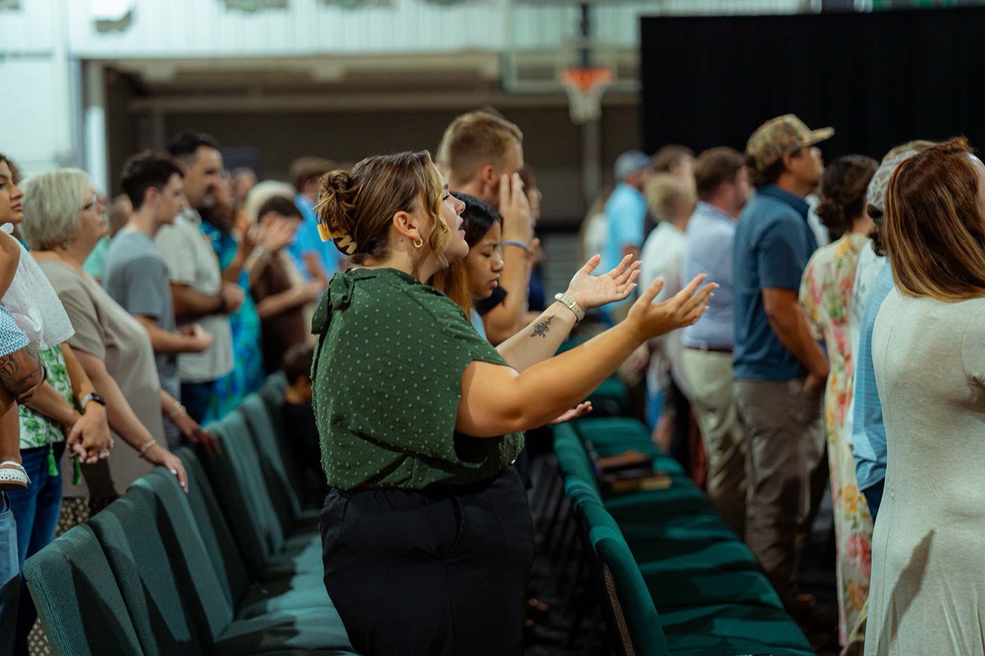 A woman standing with her hands open during worship, the congregation around her