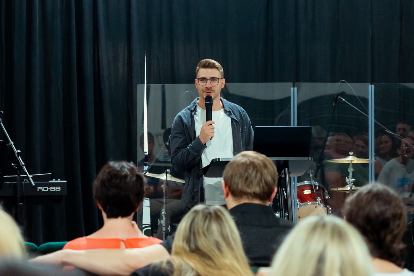 A man in a denim jacket speaking into a microphone, the congregation seated in front of him