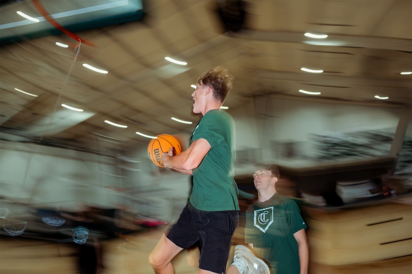 A student running with a basketball, the gym blurred with motion